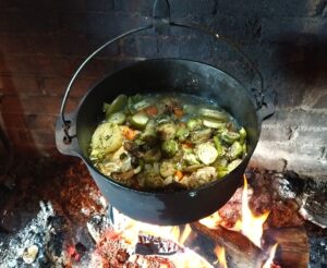 chicken stew in a cast iron pot, hanging over a fire