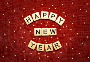 HAPPY NEW YEAR in letter tiles set against a red textured background with gold stars.