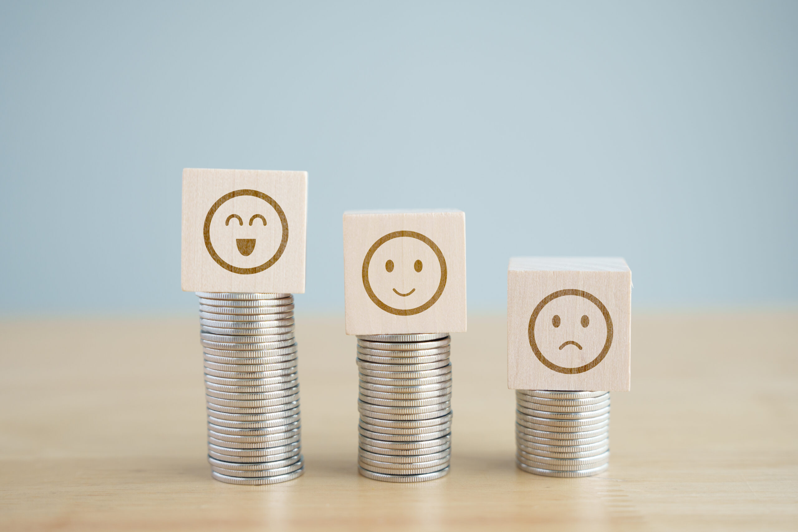 Satisfaction survey with difference of salary income or benefit or promotion position concept. Wooden block with smile face standing on high coins stack more than low level coins stack with sad face.