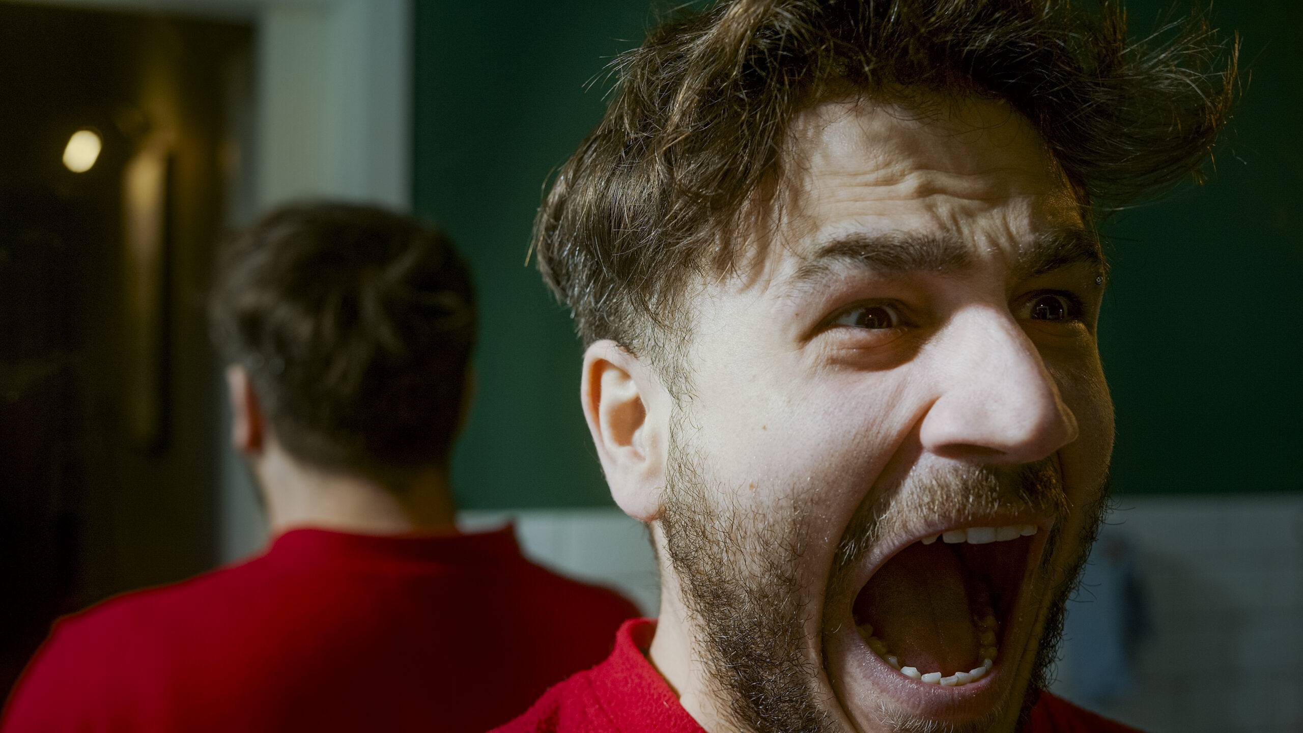 Man screaming in front of a mirror, expressing frustration, anger, or emotional distress, depicting themes of depression, inner turmoil, and personal struggle